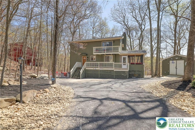 chalet / cabin with a balcony, driveway, a chimney, a storage unit, and an outbuilding