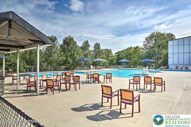 community pool featuring fence, view of wooded area, and a patio