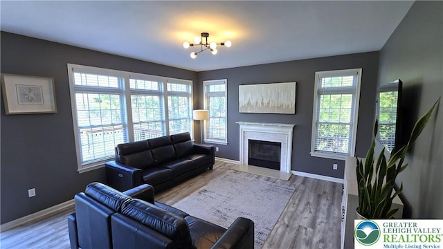 living room featuring a glass covered fireplace, a chandelier, baseboards, and wood finished floors