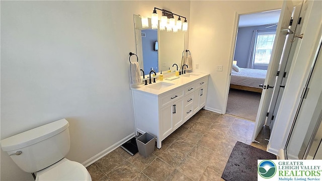 full bath with baseboards, toilet, double vanity, and stone finish floors