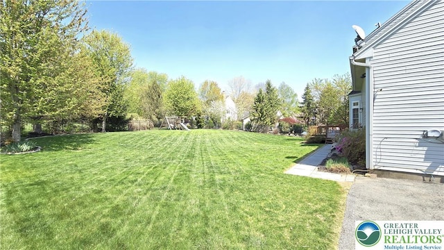 view of grassy yard with a playground and a wooden deck