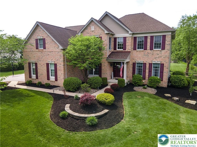 view of front of house with a front lawn, brick siding, and a shingled roof