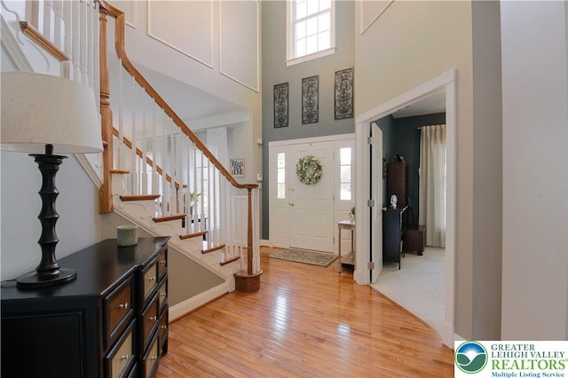 entryway with light wood-style floors, a towering ceiling, and stairs