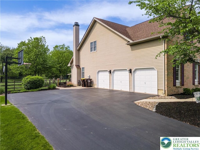 view of side of home with driveway, a chimney, a garage, and fence