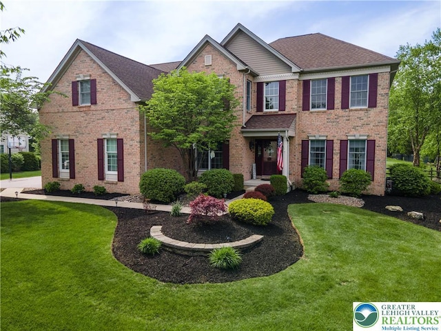view of front of home with a front lawn, brick siding, and roof with shingles