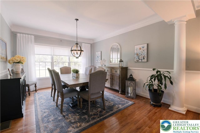 dining room featuring decorative columns, healthy amount of natural light, crown molding, wood finished floors, and a chandelier