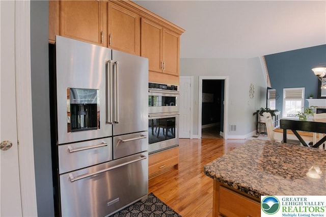 kitchen with stainless steel appliances, light wood-style flooring, dark stone counters, and baseboards