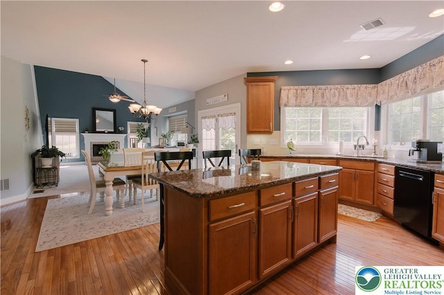 kitchen featuring black dishwasher, a sink, light wood-type flooring, a kitchen island, and vaulted ceiling