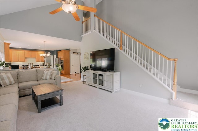 living room with light colored carpet, ceiling fan, a chandelier, stairway, and high vaulted ceiling