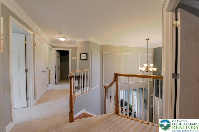 hallway with an upstairs landing, a chandelier, ornamental molding, baseboards, and carpet floors