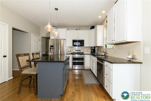 kitchen featuring appliances with stainless steel finishes, a sink, dark wood finished floors, a kitchen bar, and white cabinetry