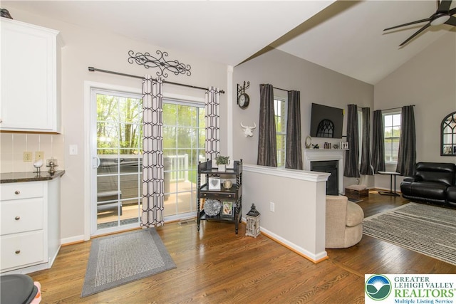 living area with light wood-style floors, a ceiling fan, a fireplace, vaulted ceiling, and baseboards