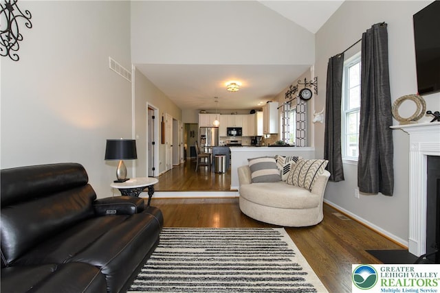 living room featuring dark wood-style floors, high vaulted ceiling, baseboards, and a fireplace with flush hearth