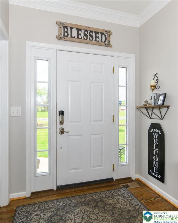 entryway with ornamental molding, dark wood-style floors, and baseboards