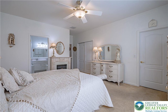 bedroom with light carpet, a closet, ceiling fan, ensuite bathroom, and a fireplace