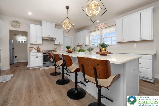 kitchen featuring stainless steel appliances, under cabinet range hood, a kitchen breakfast bar, white cabinets, and recessed lighting