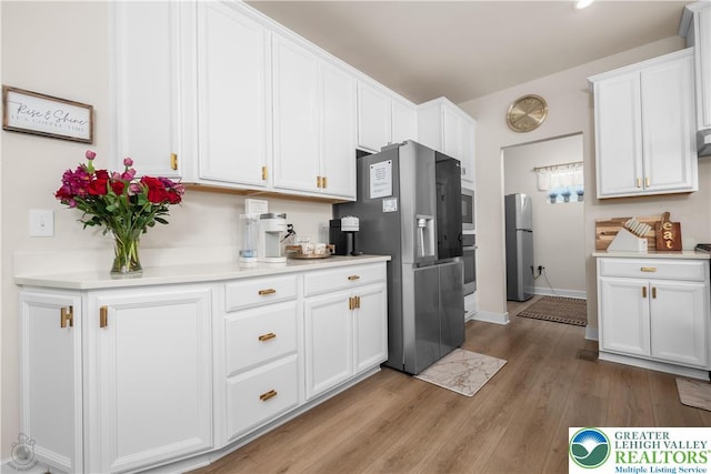 kitchen with stainless steel appliances, light countertops, white cabinets, light wood-type flooring, and baseboards