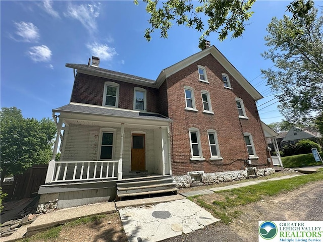 view of front facade with a chimney, brick siding, and a porch