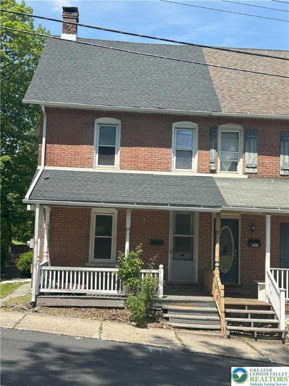 view of front of house with a porch, a chimney, and brick siding