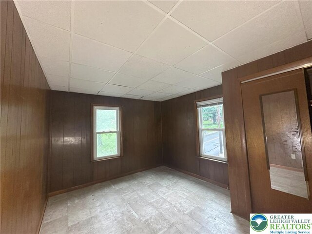 empty room with wooden walls, healthy amount of natural light, a drop ceiling, and baseboards