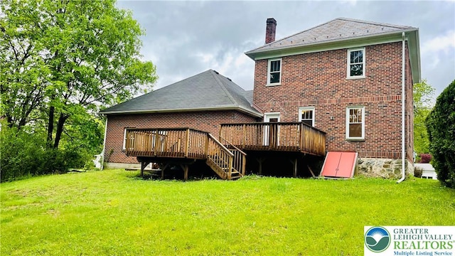 rear view of house featuring a wooden deck, a yard, brick siding, and a chimney