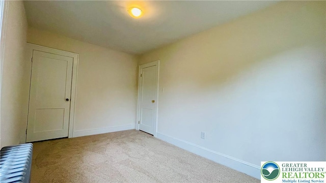 spare room featuring radiator, carpet floors, and baseboards