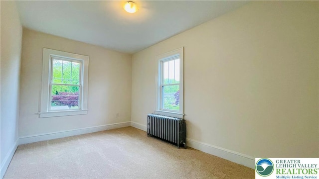 spare room with radiator, plenty of natural light, carpet flooring, and baseboards
