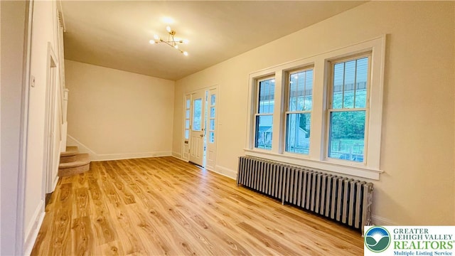 empty room featuring radiator, light wood finished floors, baseboards, stairway, and a chandelier