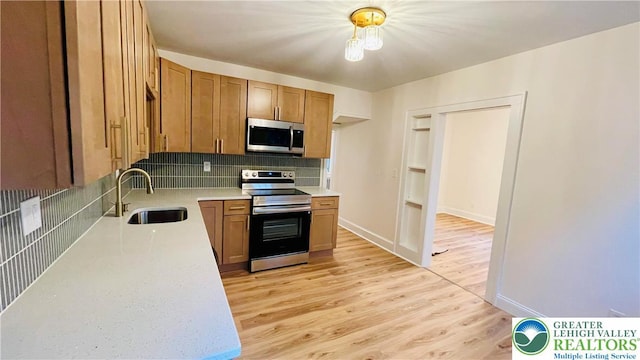 kitchen featuring appliances with stainless steel finishes, a sink, light countertops, backsplash, and light wood finished floors