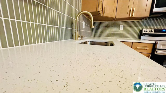 kitchen with a sink, white microwave, decorative backsplash, brown cabinets, and stainless steel electric stove