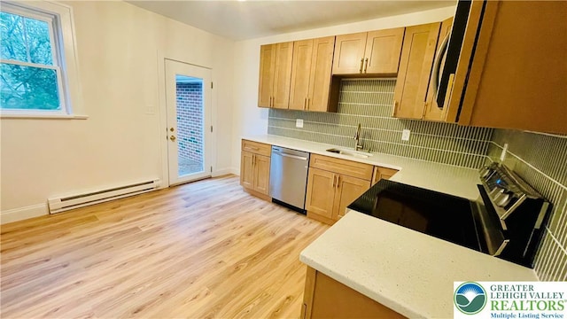 kitchen featuring appliances with stainless steel finishes, a baseboard heating unit, a sink, light wood-style flooring, and backsplash