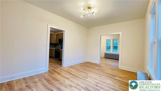 empty room with radiator, a chandelier, light wood-style flooring, and baseboards