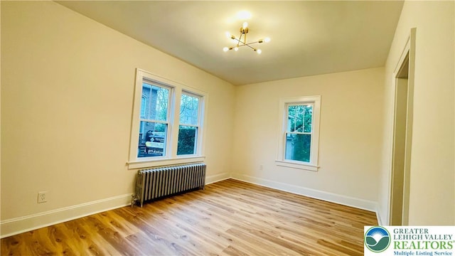 unfurnished room with radiator, a chandelier, wood finished floors, and baseboards