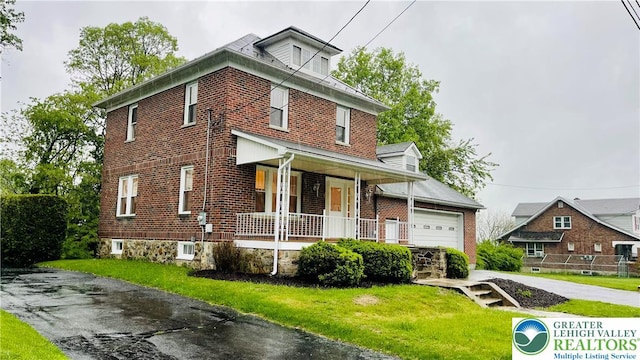 american foursquare style home featuring a porch, brick siding, a front lawn, and an attached garage