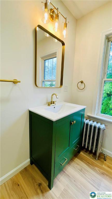 bathroom with radiator heating unit, wood finished floors, vanity, and baseboards
