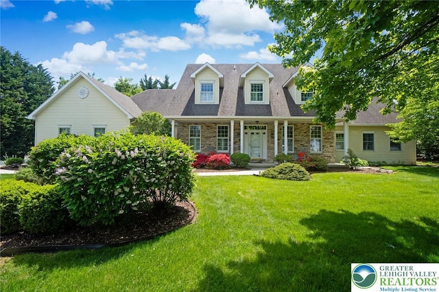 cape cod house featuring stone siding, a front lawn, a porch, and roof with shingles