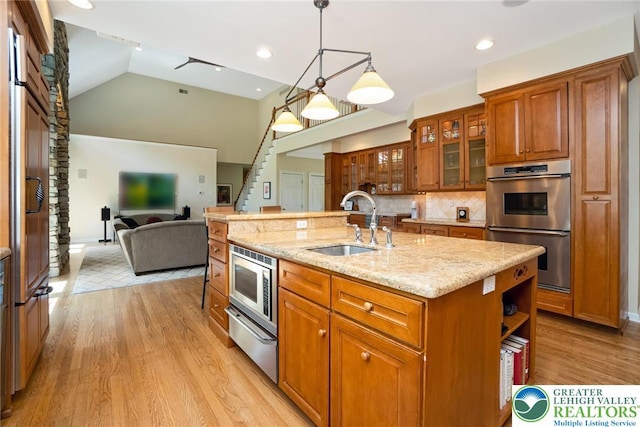 kitchen featuring a sink, stainless steel appliances, brown cabinets, a warming drawer, and light stone countertops