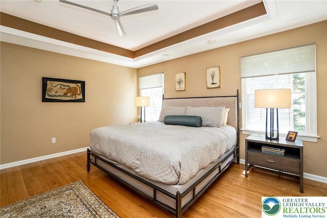 bedroom featuring a raised ceiling, light wood finished floors, baseboards, and ceiling fan