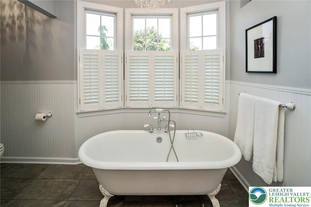 bathroom featuring wainscoting, a soaking tub, baseboards, and toilet