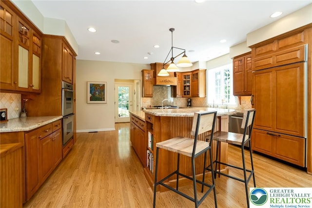 kitchen with stainless steel appliances, brown cabinetry, an island with sink, light wood-style flooring, and recessed lighting