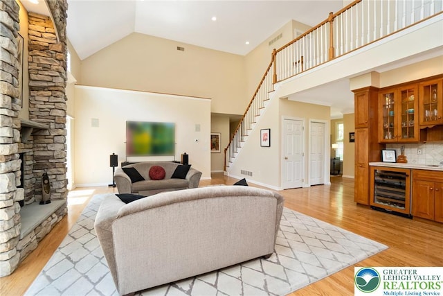 living room with beverage cooler, stairs, bar, high vaulted ceiling, and light wood-type flooring