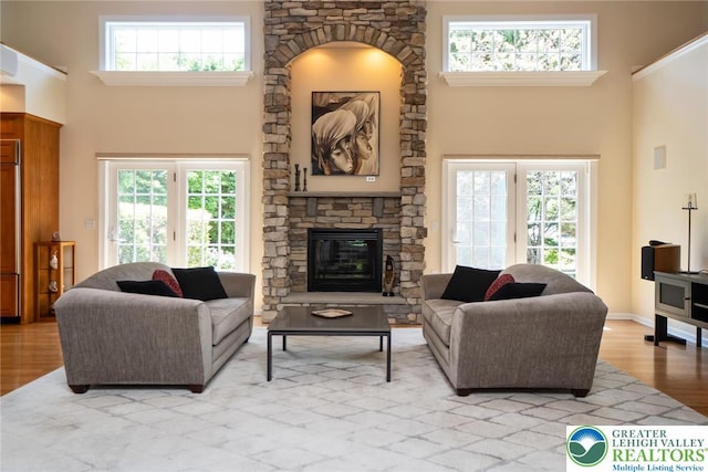 living area with light wood-type flooring, a high ceiling, a fireplace, and healthy amount of natural light