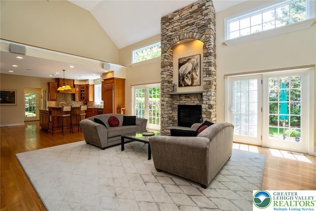 living area with high vaulted ceiling, a fireplace, and light wood-style floors