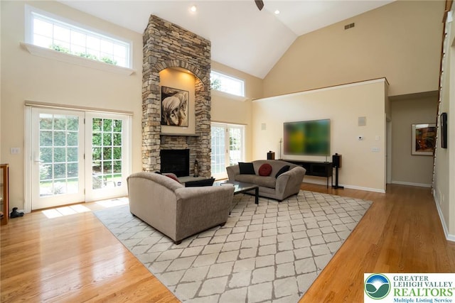 living area featuring high vaulted ceiling, a fireplace, light wood-style flooring, and baseboards