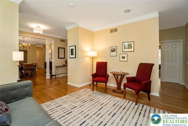 living area with a chandelier, wood finished floors, baseboards, ornamental molding, and decorative columns