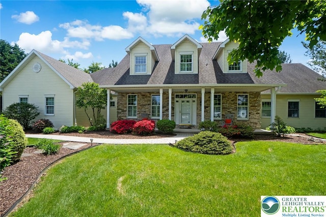 new england style home with stone siding, a front lawn, a porch, and roof with shingles