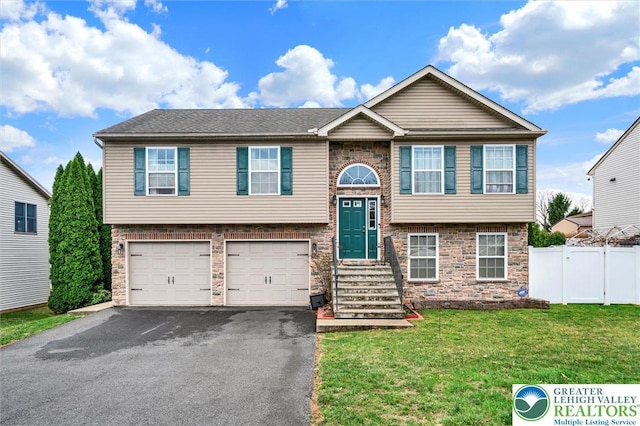 raised ranch featuring asphalt driveway, stone siding, and an attached garage