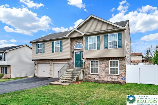 raised ranch with stone siding, asphalt driveway, a garage, and a gate