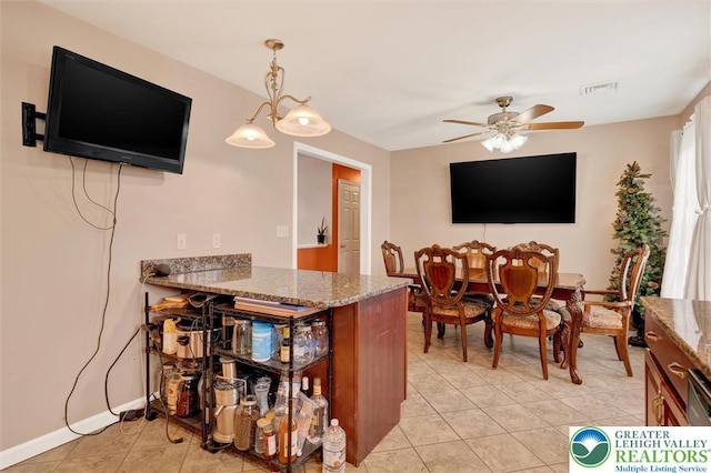 kitchen featuring light tile patterned floors, light stone counters, a ceiling fan, decorative light fixtures, and baseboards