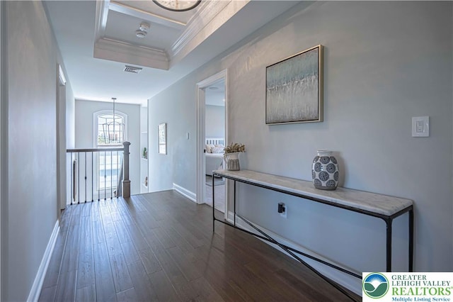 hall featuring baseboards, crown molding, dark wood finished floors, a raised ceiling, and an upstairs landing